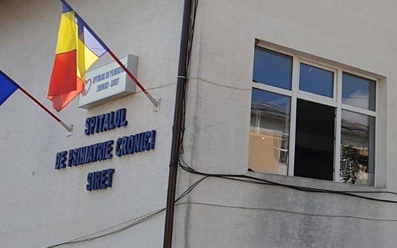 Fațada Spitalului de Psihiatrie Cronici Siret, cu numele spitalului și drapelele